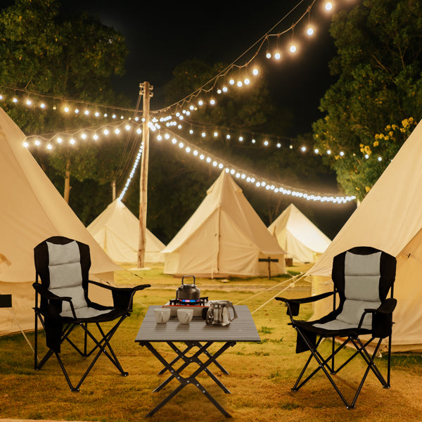 Black camping folding table between tents with evening string lights overhead