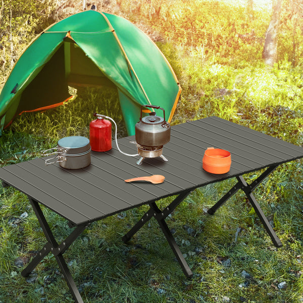 Black foldable camping table with cookware on grass near a green tent
