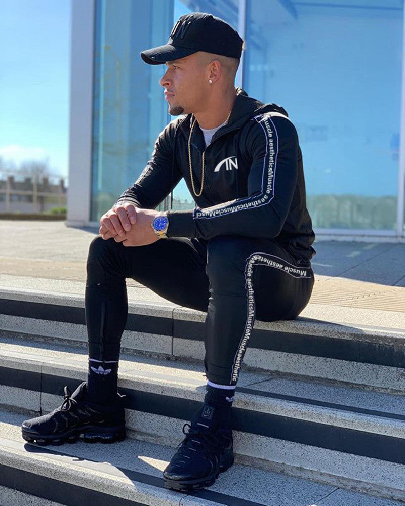 Black men’s zip-up hoodie and jogger tracksuit set with white trim along sleeves and legs.