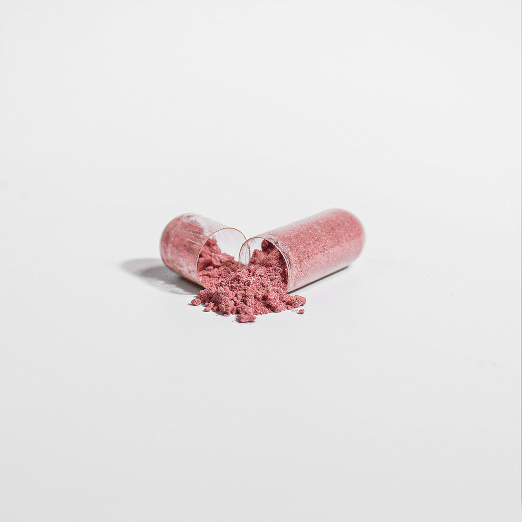 Two pink beetroot powder capsules with loose red-pink powder on surface
