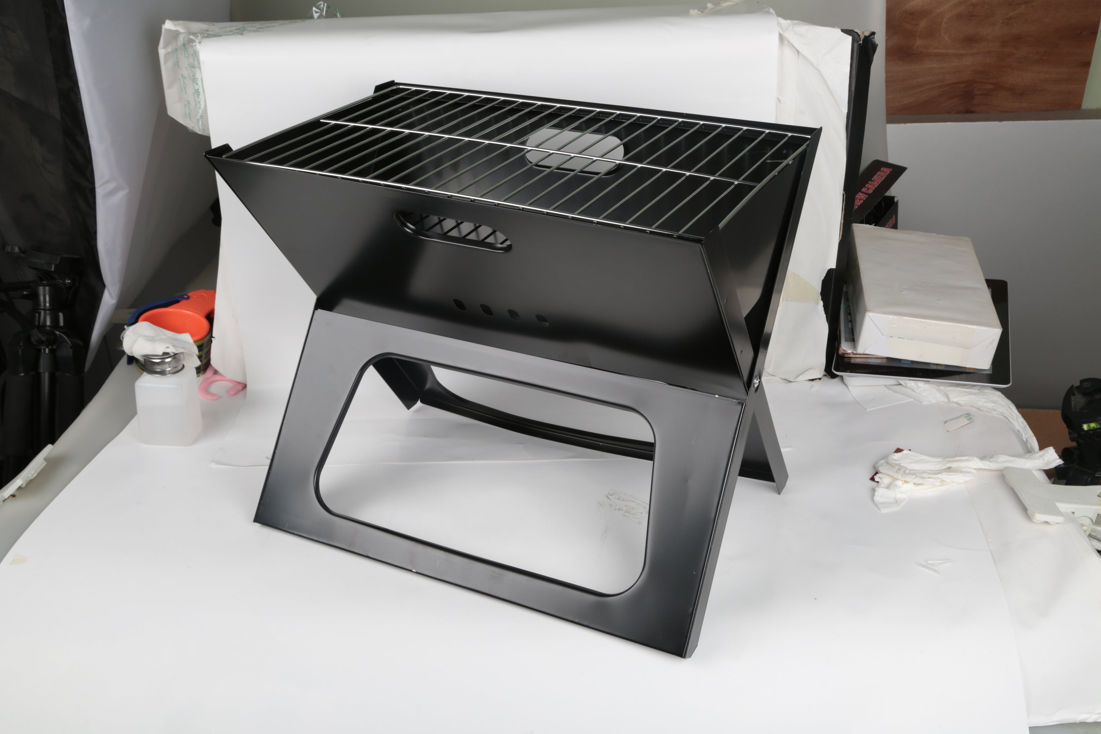 Black portable charcoal grill with wire grate and front handle opening on fold-out stand