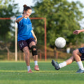 Black open-knee knee brace on soccer player’s knee; reinforced hinged support