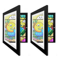 Two black front-opening A4 art frames angled open and closed, with colorful artwork inside.