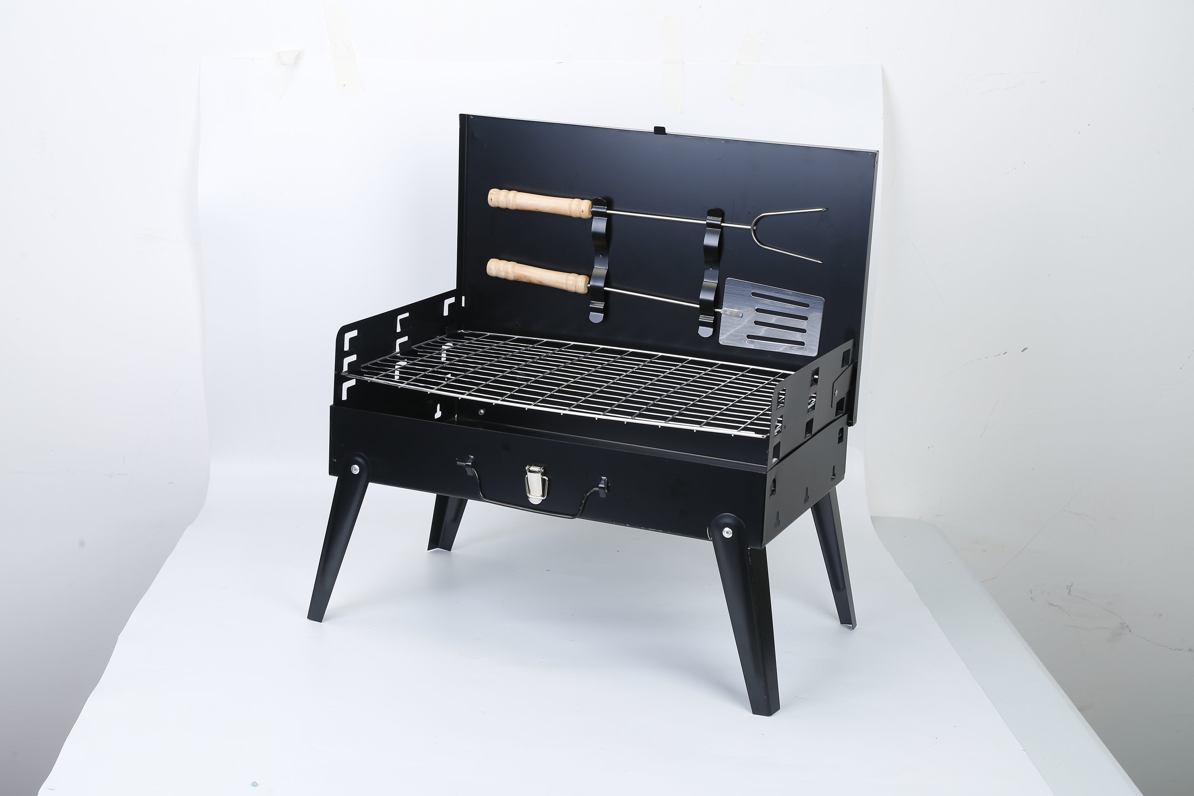 Black portable BBQ grill with lid open, wire cooking grate and attached utensil holders