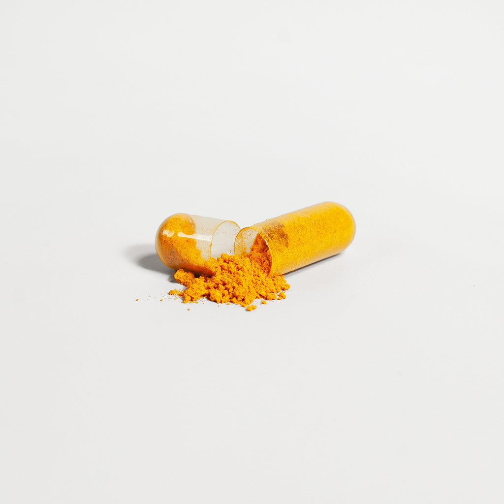 Orange turmeric powder with two split capsules beside it