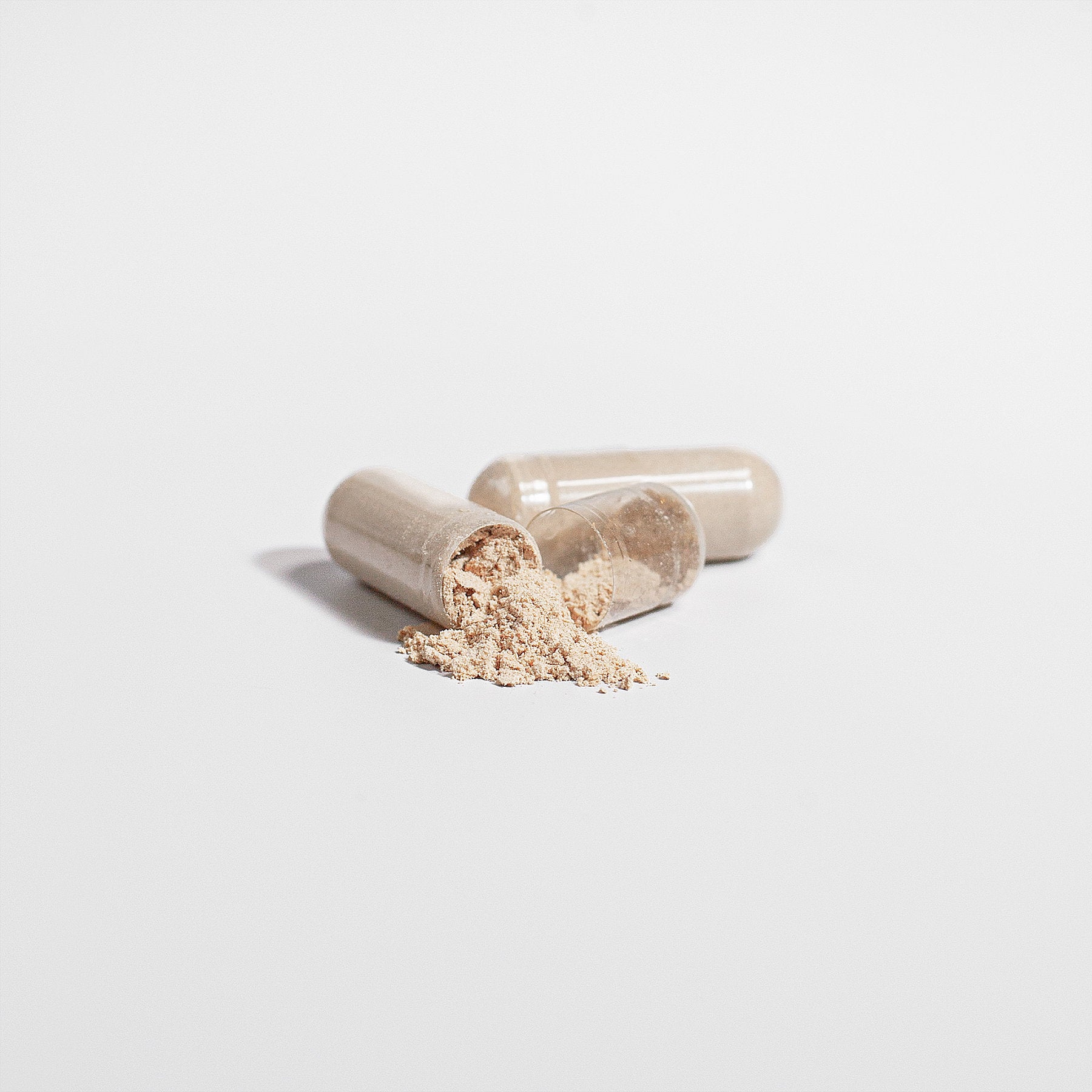 Beige vegan capsules with powdered Lion's Mane Mushroom scattered on a surface.
