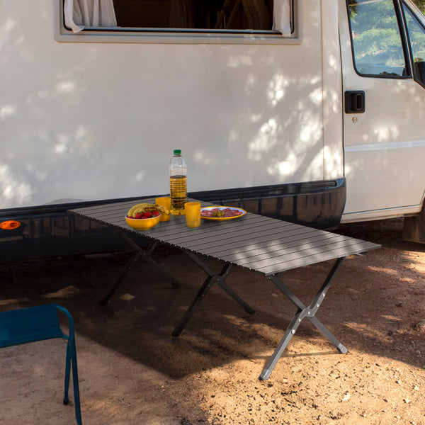 Black foldable camping table extended beside a camper van with food and drinks