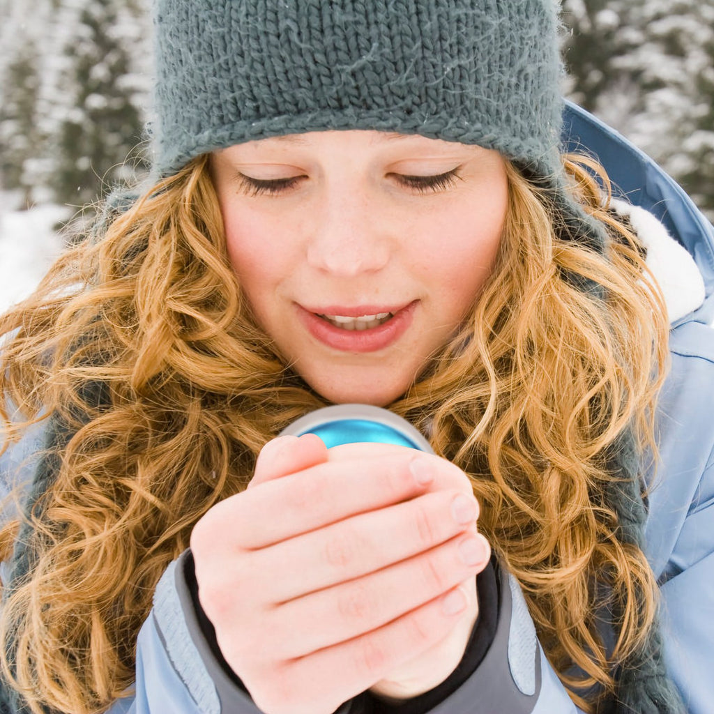 Hand warmer and power bank, blue oval held close for warmth against winter clothing.