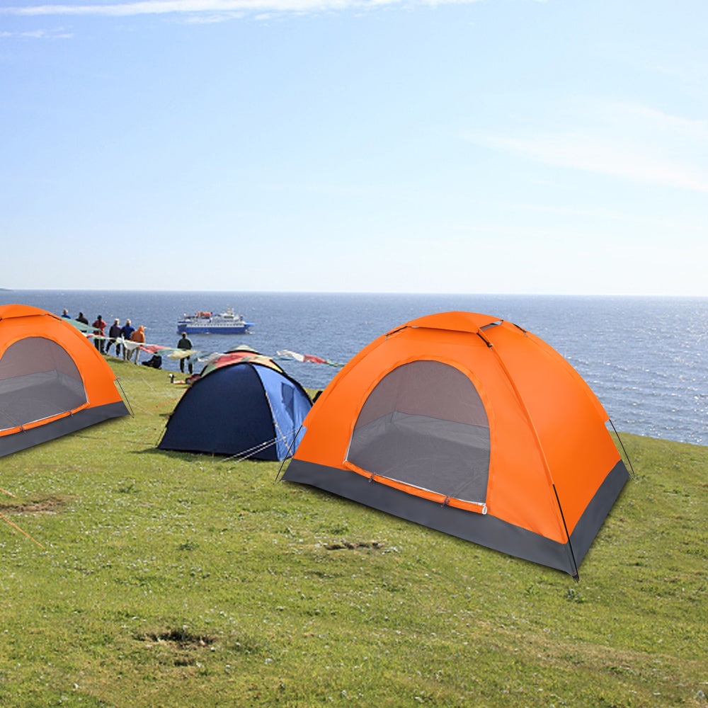 Orange 1-person dome tent on grassy campsite near the ocean