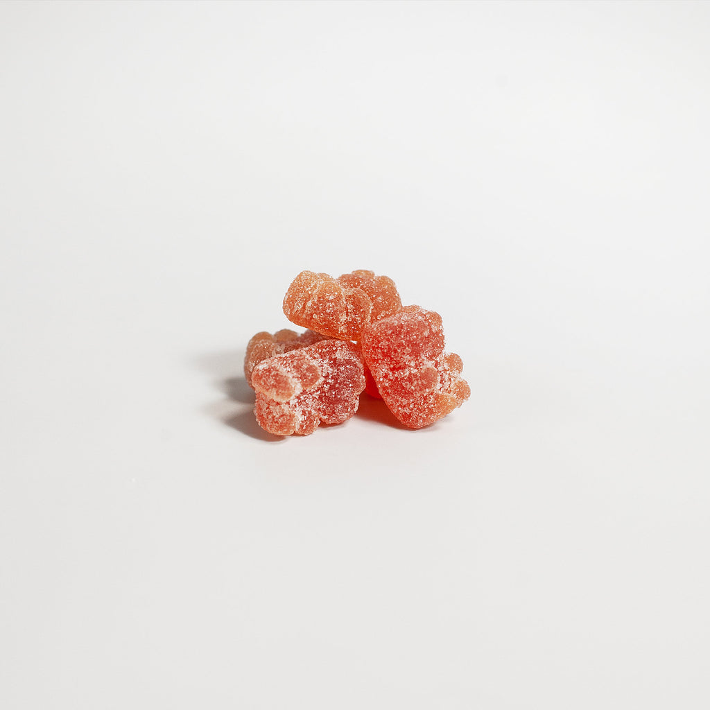 Red multivitamin gummies shaped like bears, scattered on white background