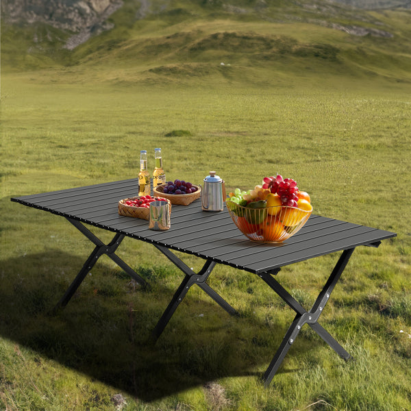Black folding camping table set up on grass with cookware and serving items
