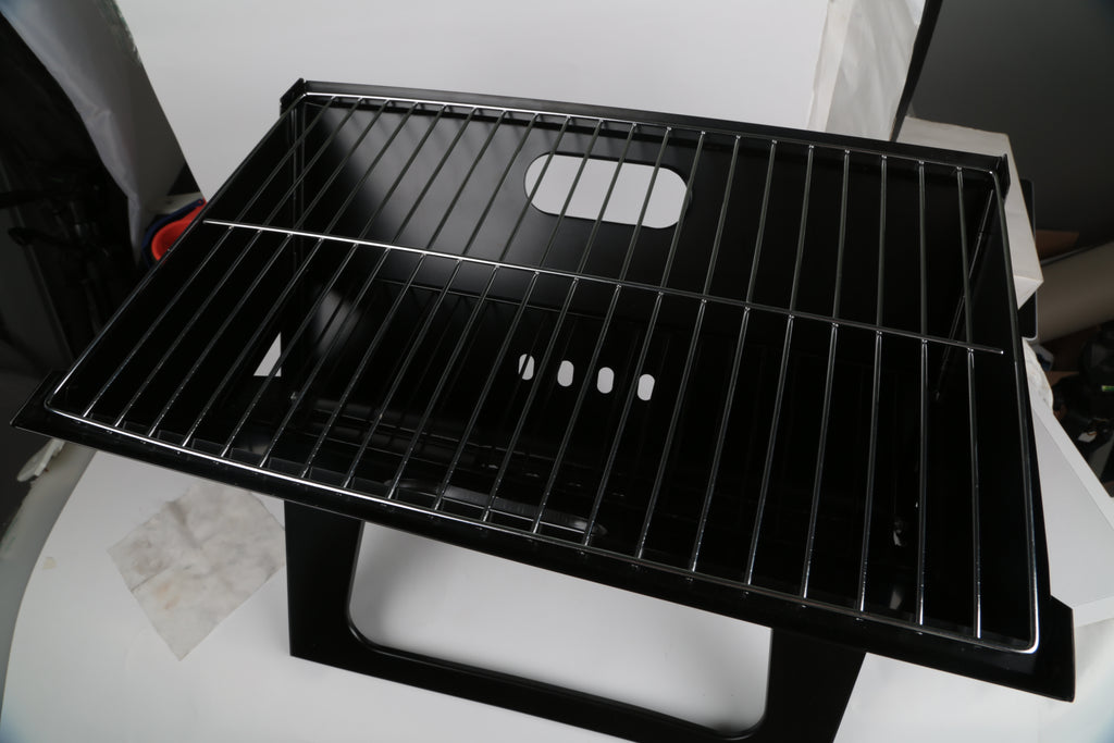 Black foldable charcoal grill with empty wire cooking grate and side vent holes