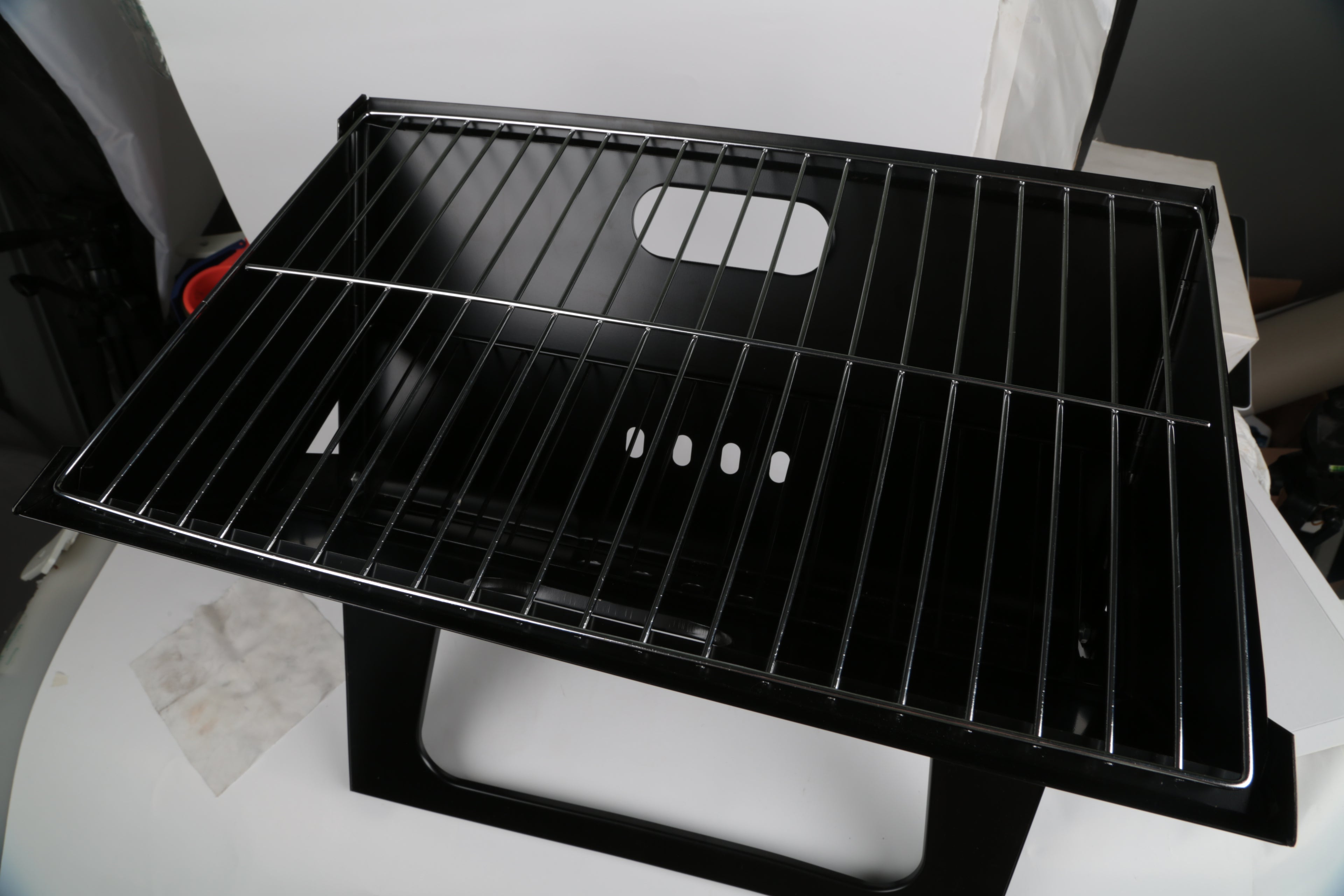 Black foldable charcoal grill with empty wire cooking grate and side vent holes